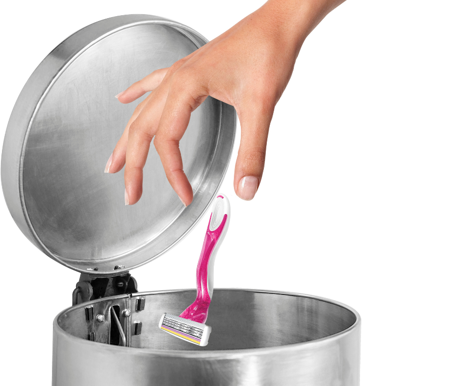 Person's hand throwing shaving razor into metal garbage can.